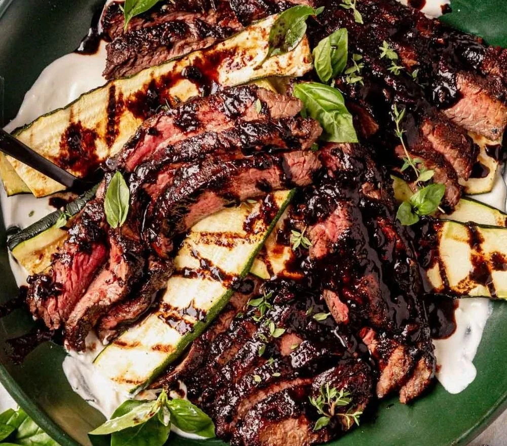 Balsamic glazed flank steak served on a platter with herbs