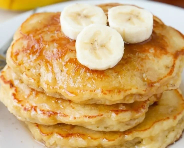Delicious homemade banana pancakes stacked on a plate with syrup and banana slices.