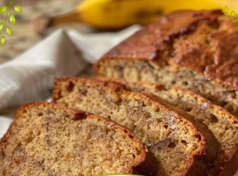 Sliced moist banana bread on a wooden board with bananas in the background