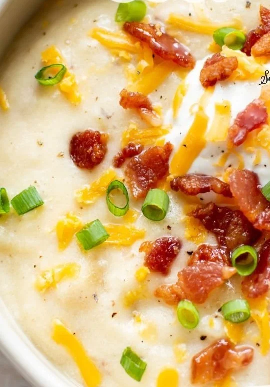 Bowl of creamy loaded potato soup topped with cheese and green onions.