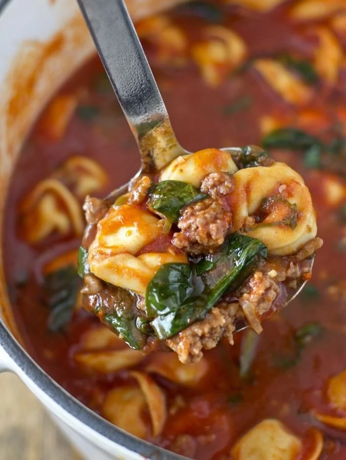 Bowl of Tortellini Soup with Italian sausage and spinach garnished with herbs