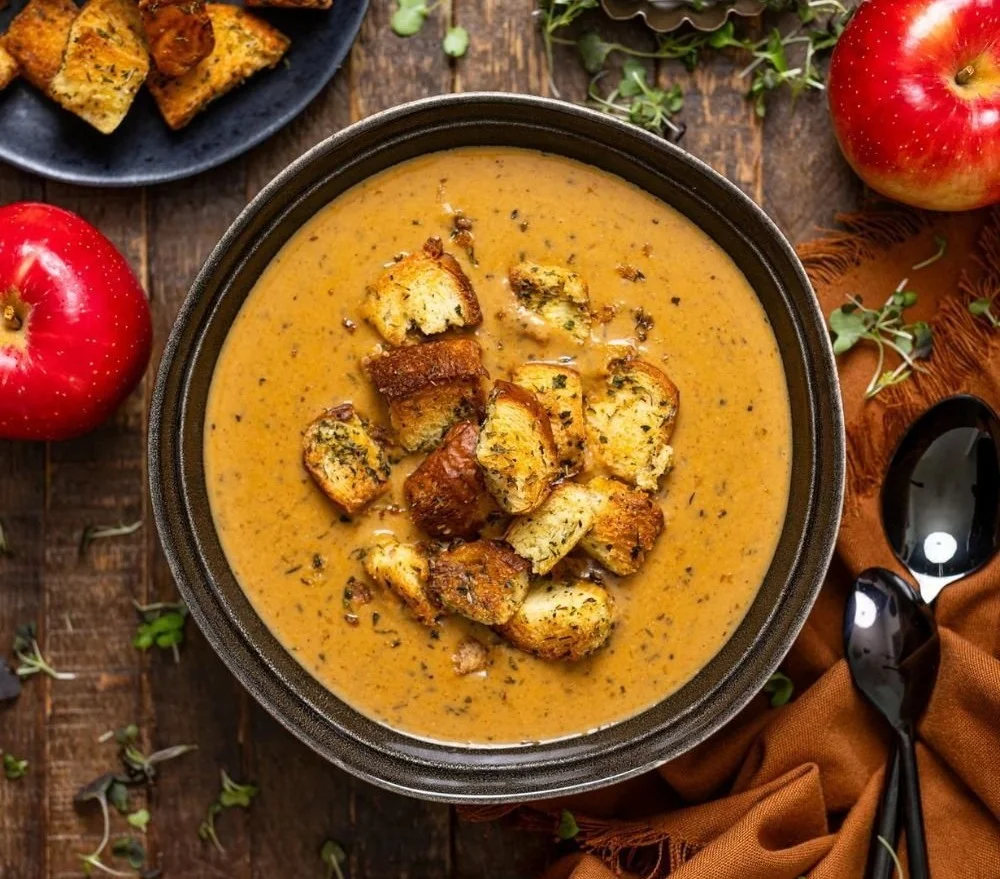 A bowl of creamy roasted apple pumpkin soup garnished with herbs.