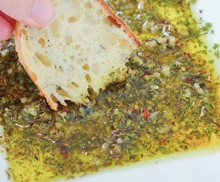 Homemade dipping oil for bread served in a bowl with herbs and spices.