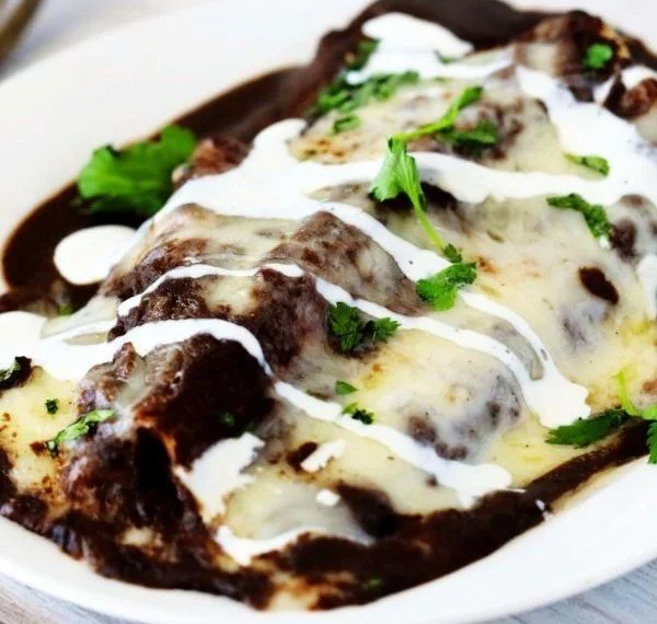 Delicious enfrijoladas topped with black bean sauce and fresh garnishes