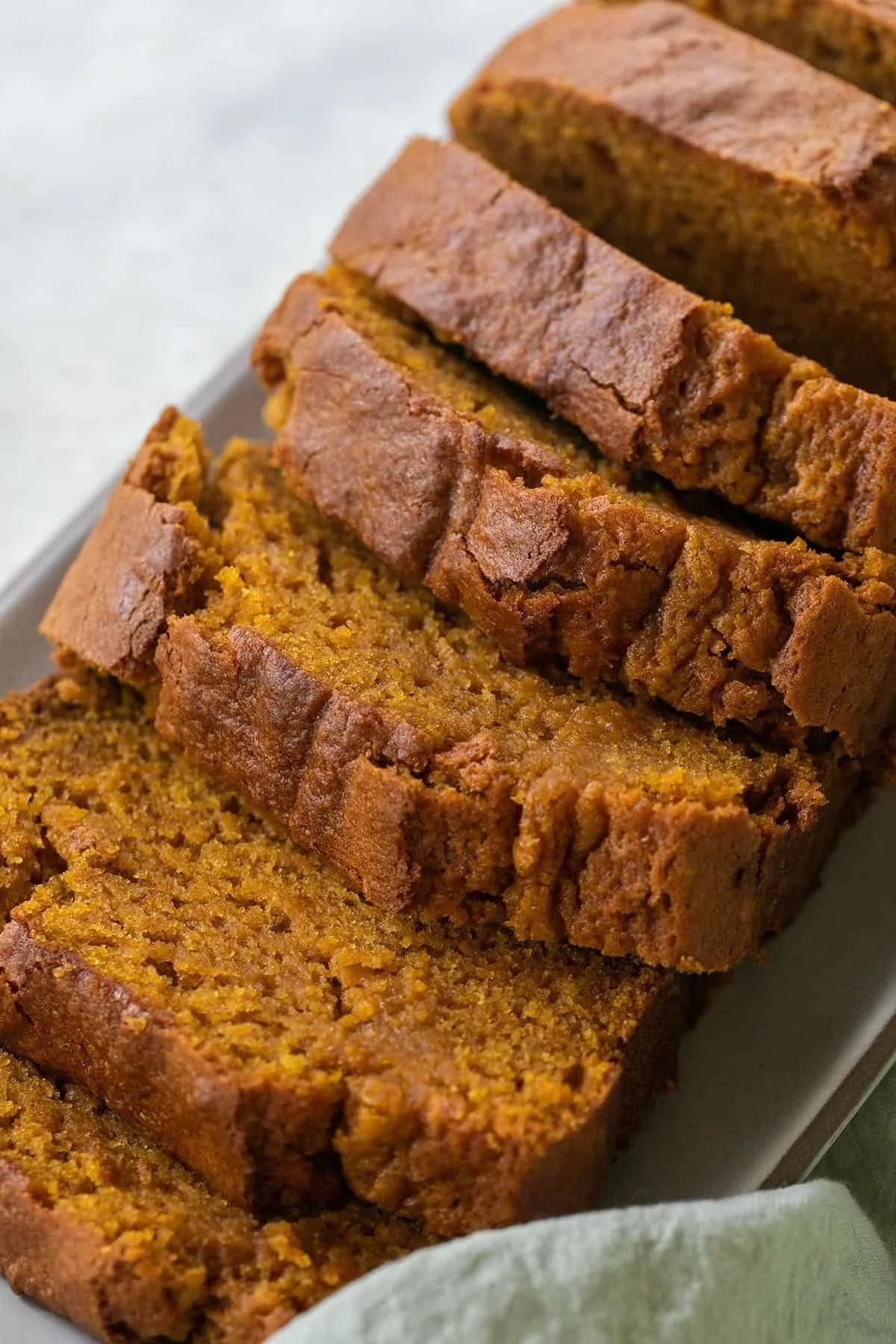 Slice of moist pumpkin bread on a wooden board with spices and pumpkin.