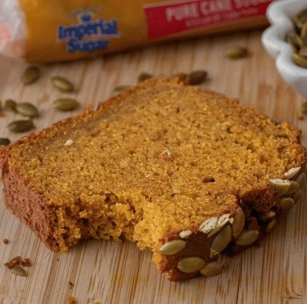 Slice of soft Starbucks pumpkin loaf on a rustic table surrounded by autumn leaves.